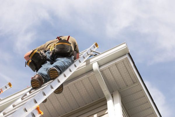 gutter A handyman repairs his rain gutters.  He is up a ladder, photo taken from ground looking up, low angle view.  He wears a tool belt, sky and clouds, good copy space.